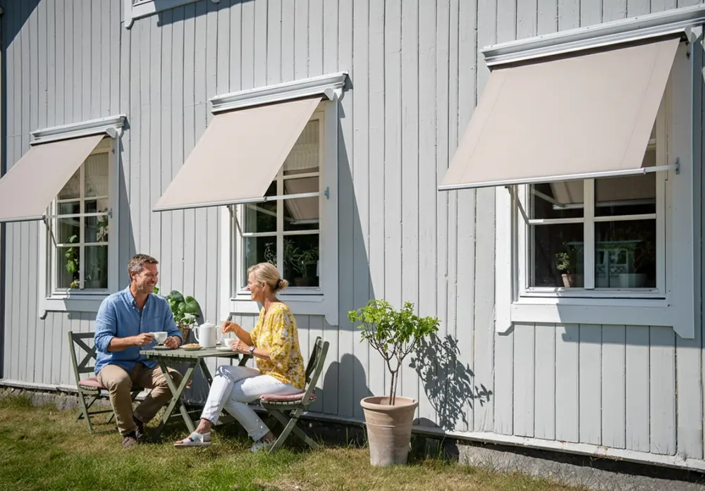 Grått trähus med vita fönstermarkiser monterade ovanför fönstren