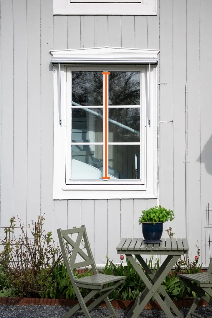 Fönster på en ljusgrå träfasad med en orange linje som markerar den höjd fönstermarkisen ska täcka